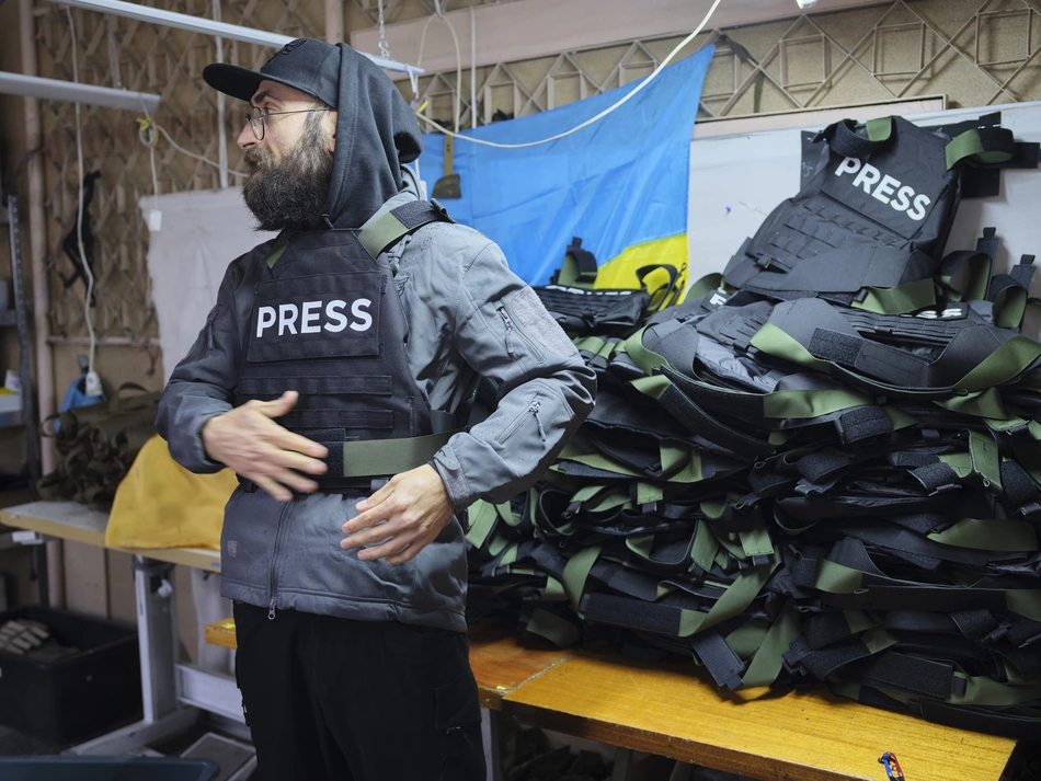 A man in a "press" vest stands in front of a pile of gear - protection for those who inform the population during the war in Ukraine.