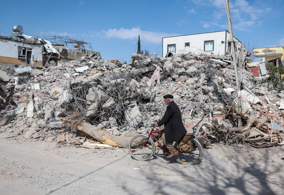 In Turkey, a man on a bicycle rides past buildings destroyed after the earthquake - need for emergency aid, reconstruction and sustainable support