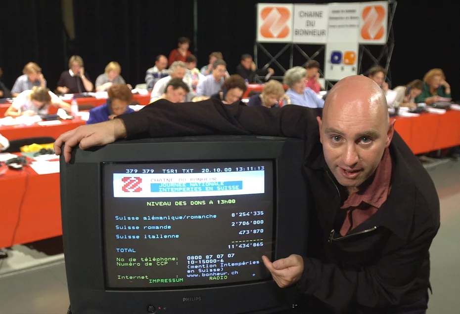 Jean-Marc Richard standing in front of a tube TV showing Teletext coverage of Swiss Solidarity.