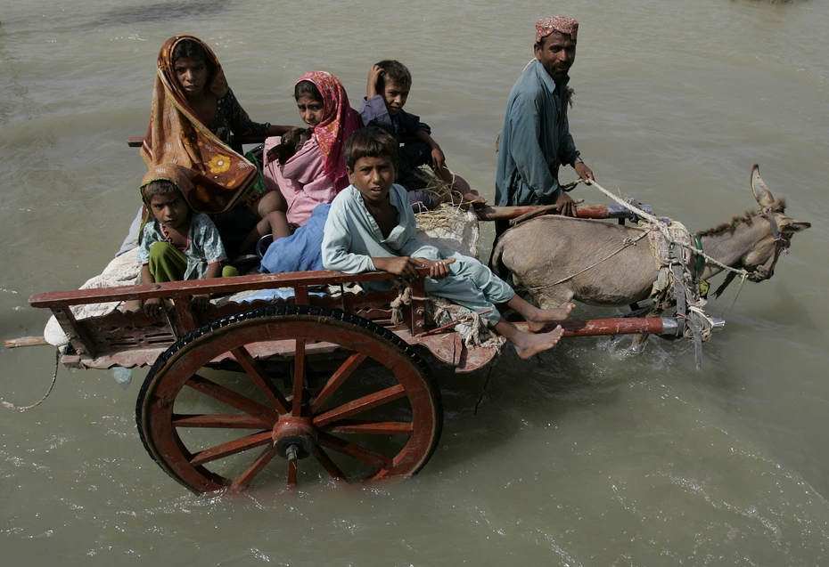 A donkey pulling a wagon with five children while a man walks beside it through flooded streets during the 2010 Pakistan floods humanitarian aid efforts.