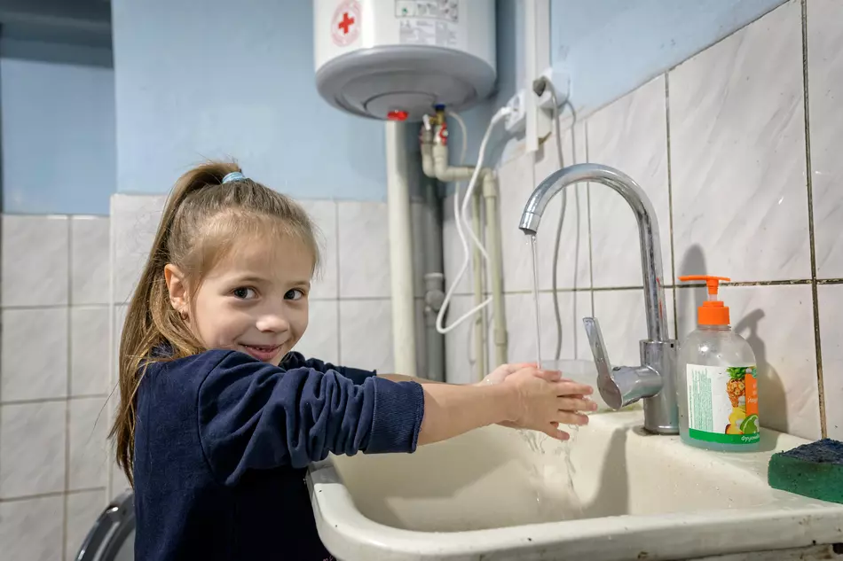 A little girl washes her hands with a smile - access to drinking water and hygiene made possible by humanitarian aid in Ukraine.