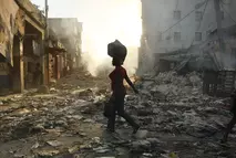 A woman walks through a destroyed town in Haiti carrying a bag on her head at sunset after the 2010 earthquake supported by Swiss Solidarity’s relief efforts.