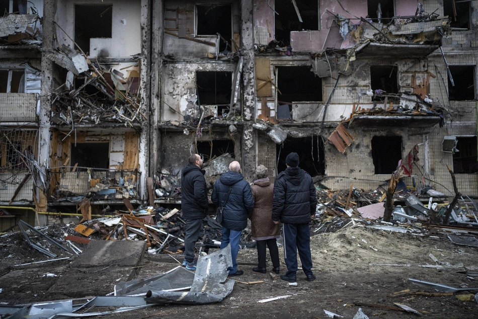 Four people look at the ruins of a damaged building in Kyiv - urgent need for humanitarian aid and reconstruction.
