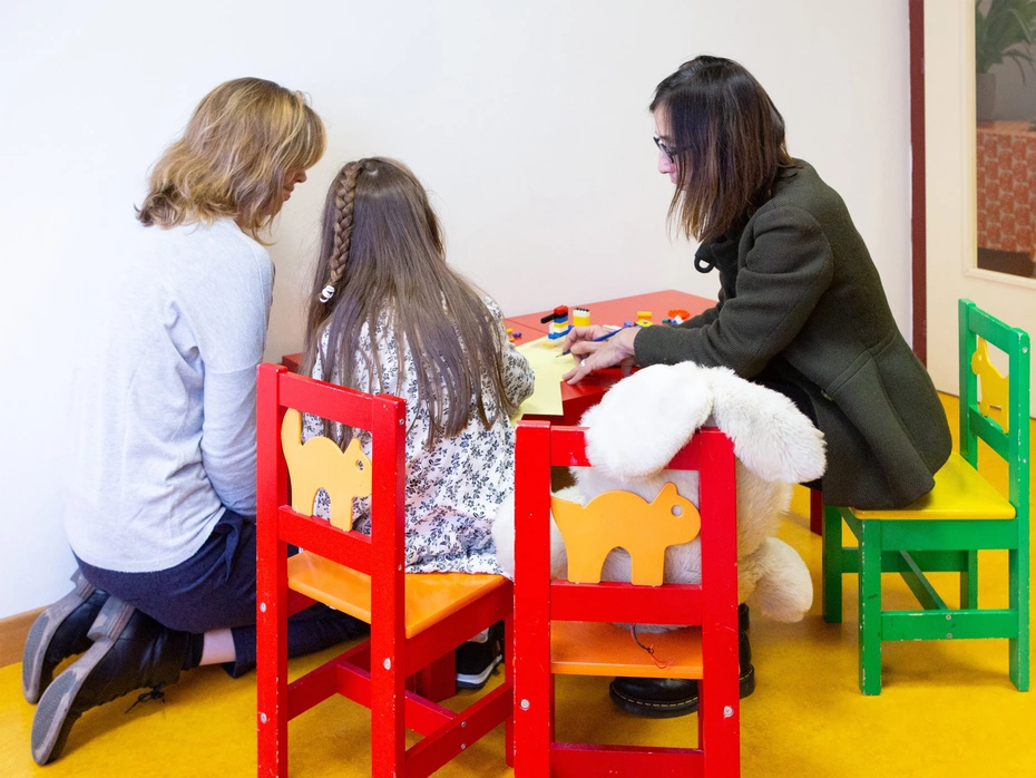A girl and two adult women sit at a small table, seen from behind.