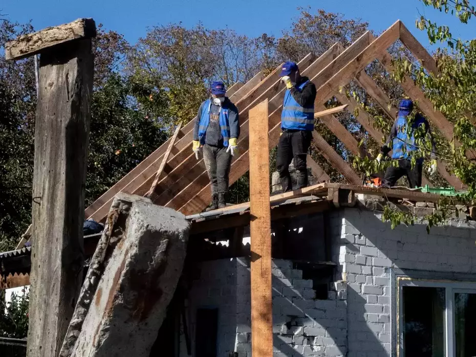 Workers repair the frame of a damaged house - reconstruction enables affected families to stay in their homes.