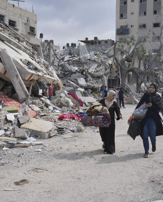Palestinian women walk past destroyed buildings in Nuseirat, Gaza - urgent need for humanitarian aid.