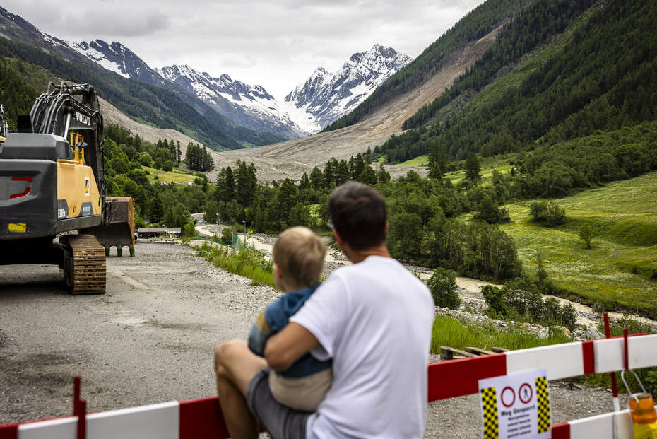 Blatten after the landslide: looking into an uncertain future Father with child looking at landslide area in Blatten - giving hope through local help and support.
