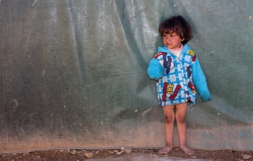 Barefoot girl standing on soily ground looking anxious – donate now to help children in need.