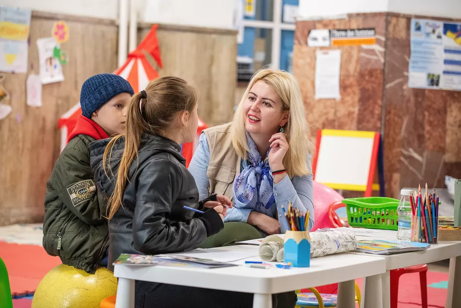 A teacher and two children in a colorful schooling room - access to education for displaced children in Ukraine despite the war.