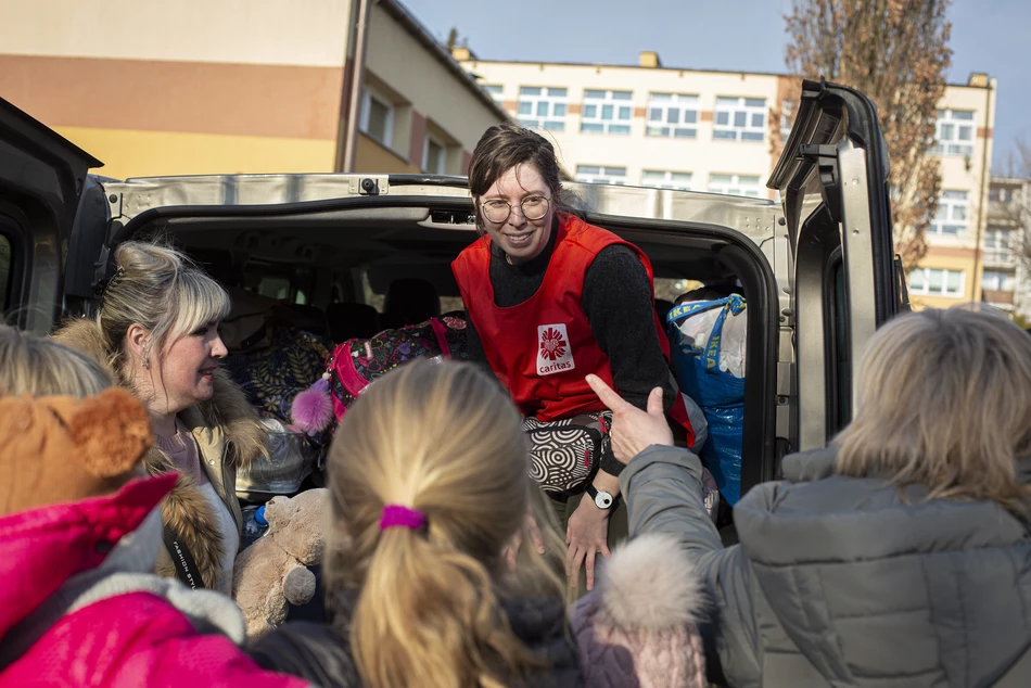A Caritas employee talks to refugee women and children near a vehicle - distributing cash aid in Odessa oblast, Ukraine.
